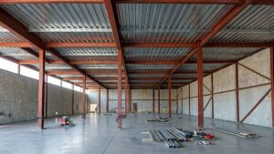 O steel deck é uma solução estrutural que substitui a laje tradicional com mais eficiência porque combina aço e concreto em um sistema único, eliminando formas convencionais, reduzindo escoramentos e acelerando o processo construtivo. Esse sistema permite maior rapidez de execução, menor desperdício de materiais e excelente desempenho estrutural, tornando-se uma das tecnologias mais modernas da construção civil, especialmente quando associado a estruturas metálicas. Cada vez mais utilizado em projetos residenciais, comerciais e industriais, o steel deck representa uma evolução na forma de construir pavimentos e coberturas. Neste guia completo, você entenderá como funciona, quais são suas vantagens, quando utilizar e por que empresas especializadas como a AGS Metálica são essenciais para garantir resultados seguros e eficientes. O que é o steel deck O steel deck é um sistema de laje mista composto por chapas de aço galvanizado perfiladas e uma camada de concreto estrutural. A chapa metálica possui dupla função: atua como fôrma durante a concretagem e, após a cura do concreto, passa a funcionar como armadura positiva da laje. Na prática, isso significa que o elemento metálico permanece incorporado à estrutura final, diferente das formas tradicionais de madeira que são removidas após a concretagem. Esse sistema normalmente inclui: • Chapas metálicas perfiladas • Concreto estrutural • Conectores de cisalhamento • Armaduras complementares quando necessário • Vigas metálicas de apoio A união entre aço e concreto cria um comportamento estrutural composto, aumentando resistência e eficiência do conjunto. Como funciona a laje steel deck O funcionamento do steel deck baseia-se na ação conjunta entre aço e concreto. Durante a execução: 1. As chapas metálicas são fixadas sobre as vigas estruturais. 2. Elas servem como plataforma de trabalho para as equipes. 3. O concreto é lançado sobre as chapas. 4. Após a cura, o aço e o concreto passam a atuar como um único elemento estrutural. Essa interação ocorre porque o perfil da chapa possui relevos e geometria específica que permite aderência ao concreto, garantindo transferência de esforços entre os materiais. O resultado é uma laje leve, resistente e com excelente desempenho estrutural. Diferença entre steel deck e laje tradicional A principal diferença entre o steel deck e a laje convencional está na metodologia construtiva. Na laje tradicional: • Utilizam-se formas de madeira ou metálicas removíveis • É necessário escoramento intenso • Há maior consumo de concreto • O tempo de execução é maior • Existe maior geração de resíduos No steel deck: • A chapa metálica substitui a forma • O escoramento é reduzido ou eliminado • O consumo de materiais é otimizado • O processo é mais rápido • O desperdício é menor Além disso, o steel deck combina resistência do concreto à compressão com resistência do aço à tração, resultando em um sistema estrutural mais eficiente que muitos métodos convencionais. Por que o steel deck substitui a laje tradicional com eficiência Existem vários fatores que tornam o steel deck uma alternativa eficiente. Eliminação de formas removíveis A chapa metálica funciona como forma permanente, dispensando madeira e reduzindo etapas construtivas. Isso reduz custos, tempo e desperdício de materiais, além de simplificar a logística do canteiro. Redução de escoramentos Em muitos casos, o steel deck dispensa escoramento intenso, o que acelera a execução e melhora a segurança da obra. Menos escoras significa mais espaço livre para circulação de trabalhadores e equipamentos. Rapidez de execução A instalação das chapas é rápida e prática, permitindo avanço acelerado da obra. Após a montagem, a laje já pode receber concreto imediatamente, reduzindo o tempo total de construção. Plataforma de trabalho imediata As chapas metálicas criam uma superfície segura para circulação das equipes logo após a instalação. Isso permite que diferentes etapas da obra ocorram simultaneamente, aumentando a produtividade. Menor peso estrutural O steel deck possui excelente relação resistência-peso, sendo mais leve que lajes maciças tradicionais. Essa característica reduz cargas sobre fundações e estruturas, podendo gerar economia em toda a obra. Vantagens estruturais do steel deck O desempenho estrutural é um dos principais motivos da popularidade desse sistema. Entre as vantagens estão: • Alta resistência mecânica • Maior capacidade de carga • Possibilidade de maiores vãos • Redução de fissuras • Melhor comportamento estrutural global A combinação entre aço e concreto cria uma laje mais leve e resistente que sistemas convencionais. Isso permite projetos mais eficientes e econômicos. Economia de materiais e redução de custos O steel deck contribui para economia de várias formas. Primeiro, reduz o consumo de concreto, pois o perfil metálico diminui o volume necessário em comparação com lajes maciças. Segundo, elimina custos com formas removíveis e parte da mão de obra associada. Terceiro, reduz desperdícios e retrabalho. A soma desses fatores pode gerar economia significativa no custo global da obra. Sustentabilidade na construção A sustentabilidade é um diferencial importante do steel deck. O sistema gera menos resíduos, utiliza menos madeira e permite uso de aço reciclável, reduzindo impacto ambiental. Além disso, a eficiência construtiva reduz consumo de recursos e energia durante a execução. Essas características tornam o steel deck alinhado com práticas modernas de construção sustentável. Segurança durante a execução A segurança no canteiro também melhora com o uso do steel deck. A plataforma metálica cria superfície estável para circulação, reduzindo riscos de acidentes. A redução de escoramentos e materiais soltos também contribui para um ambiente mais organizado e seguro. Aplicações do steel deck em projetos residenciais Embora muito utilizado em edifícios comerciais e industriais, o steel deck também é excelente para residências. Entre as aplicações estão: • Pavimentos superiores de casas • Mezaninos • Varandas estruturais • Garagens • Coberturas acessíveis • Ampliações e reformas Residências com estrutura metálica se beneficiam ainda mais desse sistema, pois ele se integra perfeitamente ao projeto estrutural. Integração com estruturas metálicas O steel deck apresenta desempenho máximo quando utilizado em conjunto com estruturas metálicas. Isso ocorre porque ambos os sistemas compartilham características como: • Precisão dimensional • Rapidez de montagem • Industrialização do processo • Redução de peso • Alta resistência Essa integração é uma das especialidades de empresas como a AGS Metálica, que atuam desde o projeto até a execução estrutural. Conforto térmico e acústico Quando corretamente dimensionado e combinado com materiais de isolamento, o steel deck pode apresentar excelente desempenho térmico e acústico. O sistema permite inclusão de: • Mantas acústicas • Contrapisos específicos • Revestimentos técnicos Isso garante conforto equivalente ou superior às lajes tradicionais. Durabilidade e vida útil O aço galvanizado utilizado no steel deck possui alta resistência à corrosão, especialmente quando protegido e especificado corretamente. A durabilidade do sistema é elevada, podendo acompanhar toda a vida útil da edificação com manutenção mínima. Além disso, o concreto protege o aço após a cura, aumentando ainda mais a resistência do conjunto. Flexibilidade arquitetônica Outro grande benefício do steel deck é a liberdade arquitetônica. O sistema permite: • Vãos maiores • Menor número de pilares • Layouts mais abertos • Soluções arquitetônicas modernas Isso possibilita projetos mais sofisticados e personalizados. Quando o steel deck é mais indicado O uso do steel deck é especialmente recomendado em situações como: • Obras com prazo reduzido • Projetos com estrutura metálica • Construções com grandes vãos • Reformas e ampliações • Obras com necessidade de redução de peso • Empreendimentos que buscam sustentabilidade Cada projeto deve ser avaliado tecnicamente para garantir a melhor solução estrutural. Comparação entre steel deck e laje maciça Uma comparação simples ajuda a entender as diferenças. Steel deck: • Execução rápida • Menor peso • Menos desperdício • Menor escoramento • Alta resistência • Integração com estrutura metálica Laje maciça tradicional: • Execução mais lenta • Maior consumo de concreto • Maior peso estrutural • Necessidade de formas removíveis • Mais etapas construtivas Na maioria dos casos modernos, o steel deck apresenta melhor relação custo-benefício. Importância do projeto estrutural especializado Apesar das vantagens, o steel deck exige engenharia especializada. O dimensionamento correto depende de fatores como: • Vão estrutural • Cargas previstas • Tipo de perfil metálico • Espessura do concreto • Conectores estruturais • Normas técnicas aplicáveis Por isso, a escolha de uma empresa experiente é fundamental para segurança e desempenho. O papel da AGS Metálica na execução de steel deck Empresas especializadas como a AGS Metálica possuem conhecimento técnico e experiência para garantir que o steel deck seja executado com máxima eficiência. Entre os diferenciais estão: • Projeto estrutural preciso • Fabricação de componentes metálicos • Equipe técnica qualificada • Cumprimento de normas técnicas • Otimização de custos e prazos Essa expertise é essencial para que todas as vantagens do sistema sejam plenamente aproveitadas. O futuro das lajes na construção civil A tendência global da construção civil é a industrialização dos processos, buscando maior produtividade, sustentabilidade e previsibilidade. O steel deck representa exatamente essa evolução, substituindo métodos tradicionais por soluções mais inteligentes e eficientes. Com o crescimento das estruturas metálicas no Brasil, a adoção do steel deck tende a aumentar ainda mais nos próximos anos. Conclusão O steel deck substitui a laje tradicional com eficiência porque combina aço e concreto em um sistema estrutural único que elimina formas removíveis, reduz escoramentos, acelera a execução e melhora o desempenho estrutural. Essa tecnologia oferece vantagens como rapidez de obra, economia de materiais, sustentabilidade, segurança e flexibilidade arquitetônica, tornando-se uma das soluções mais modernas da construção civil. Quando executado por empresas especializadas como a AGS Metálica, o steel deck proporciona resultados superiores em qualidade, prazo e eficiência, sendo uma escolha estratégica para projetos residenciais e comerciais que buscam inovação e alto desempenho estrutural. Se desejar, posso criar também outro artigo para a AGS Metálica sobre estrutura metálica residencial, galpões metálicos ou comparativos de custo entre steel deck e laje convencional.